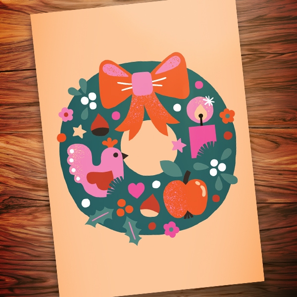 Pöydän päällä oleva joulukortti, jossa on värikäs joulukranssi