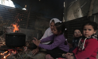 Nainen, joka istuu pimeässä lasten kanssa. Edessä on kattila nuotion päällä.