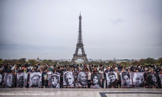 Joukko ihmisiä Eiffel-torni takanaan horisontissa pitelemässä suuria valokuvia ihmisoikeuspuolustajista.
