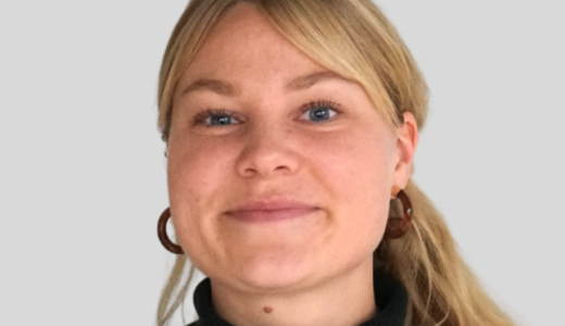 Vaaleahiuksinen ja sinisilmäinen hymyilevä nainen.