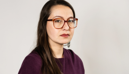 Vakavakatseinen ninen, jolla on tummat hiukset, punatut huulet ja silmälasit.