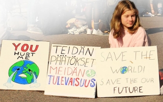 Nuori henkilö istuu maassa kolmen kyltin kanssa, joissa lukee: "You hurt me", "Teidän päätökset, meidän tulevaisuus" ja "Save the world! Save our future."