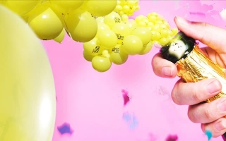 Kuvassa avautuva kuohuviinipullo, josta pulppuaa keltaisia Amnesty-ilmapalloja.