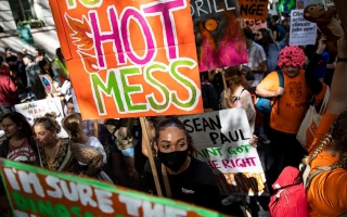 Ilmastomielenosoituksen osallistujia. Etualalla nuori henkilö mustassa maskissa ja kyltin kanssa, jossa lukee "Hot mess"