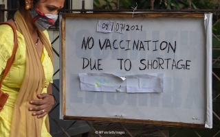 Nainen kyltin edessä, joka kertoo ettei rokotuksia ole jäljellä