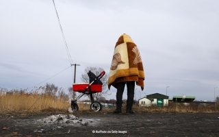 Kuva Puolan ja Ukrainan rajalta. Kuvassa on ihminen, joka on kietoutunut vilttiin. Hänen vieressään on lastenvaunut.