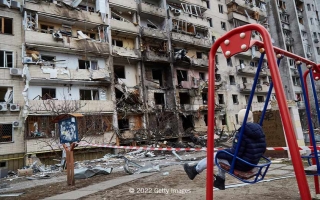 Lapsi punaisessa keinussa pommitetun asuinrakennuksen edustalla Ukrainassa.