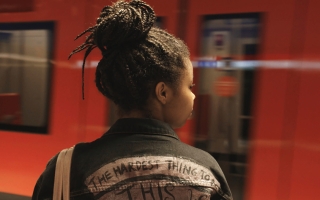 Nuori nainen katsoo asemalle saapuvaa metrojunaa, kuvattu takaapäin.