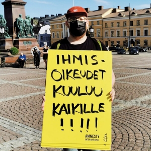 Konsta Hyötylä pitää käsissään kylttiä, jossa lukee "Ihmisoikeudet kuuluu kaikille!!!". Konsta seisoo torilla ja hänellä on musta kasvomaski. 