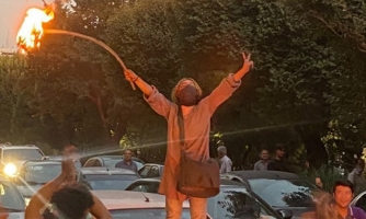 Mielenosoittaja seisoo kädet levällään. Hänellä on kädessään keppi, jonka päässä on palava hijab.