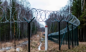 Aita Latvian ja Valko-Venäjän rajalla. Metalliaidassa on mustat tolpat ja piikkilankaa. Taustalla on metsää.