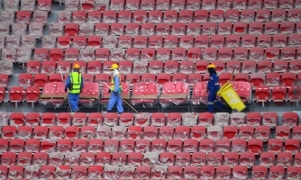 Stadionin katsomo, jossa kolme työntekijää kävelee penkkirivien välissä.