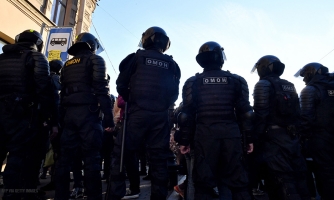 Mustiin varusteisiin pukeutuneet poliisit seisovat tiiviissä rivissä selin kameraan. Varusteiden selässä lukee valkoisella tunnus OMOH.