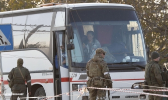 Paikallaan olevassa bussissa on ihmisiä ja sen edessä seisoo sotilaita.