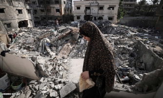 Päähuiviin pukeutunut ihminen seisoo keskellä tuhoutuneen kerrostalon raunioita.