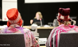 Saamelaiskäräjien istunto käynnissä, kaksi naispuolista osallistujaa kuvattuna takaapäin.