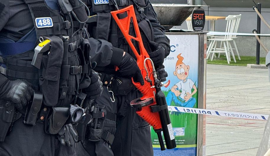 Paineilma-ase FN 303. Poliisi pitää kädessään suurta oranssia asetta.